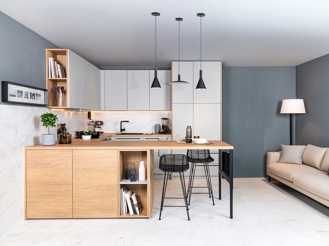 Eine moderne, offene Küche mit angrenzendem Wohnbereich, ausgestattet mit hellen Holzschränken, weißen Arbeitsplatten, grauen Wänden und einem Sofa.
