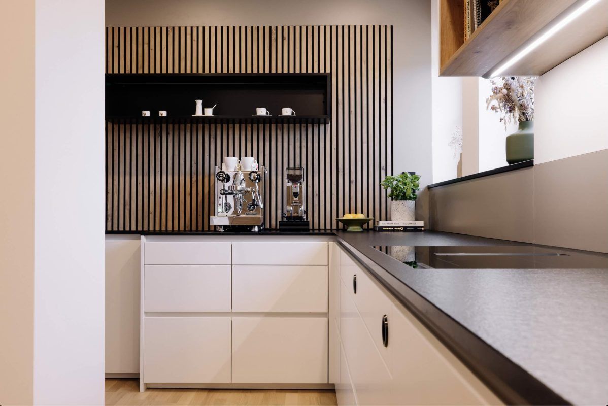 Moderne Küche mit weißen Schränken, dunkler Arbeitsplatte und einer Rückwand aus Holzlamellen mit einem schwebenden schwarzen Regal.