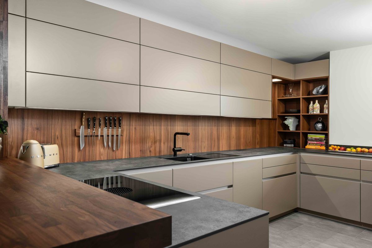 Moderne U-förmige Küche mit hellbeigen Schränken, dunkler Holzrückwand und dunkler Steinarbeitsplatte.