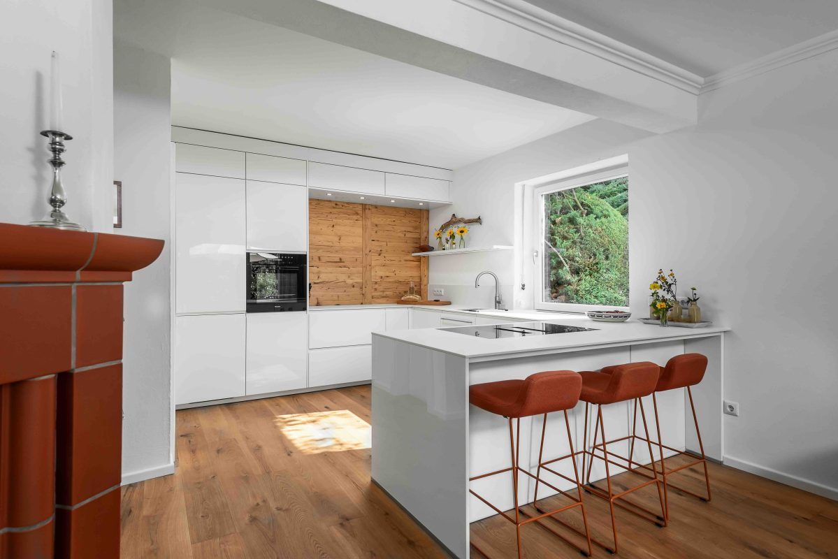 Moderne Küche mit weißen Schränken, einer Akzentwand aus Holz, einer Kochinsel mit orangefarbenen Barhockern und Holzboden.