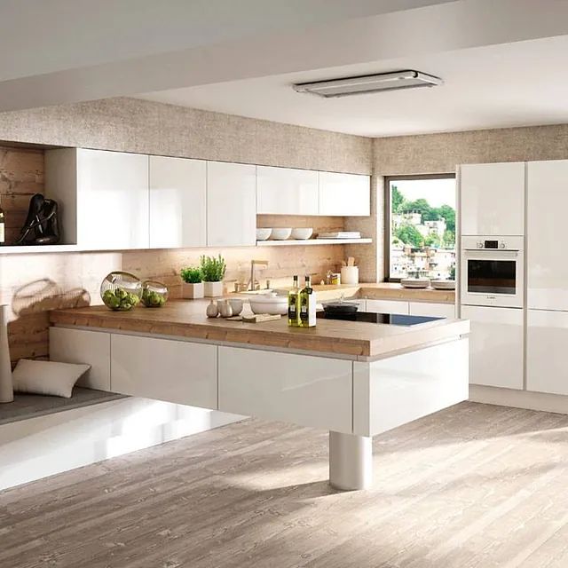 Eine moderne Küche mit weißen Hochglanzschränken, einer hellen Holzarbeitsplatte und einer schwebenden Halbinsel, die von einer einzelnen Säule getragen wird.