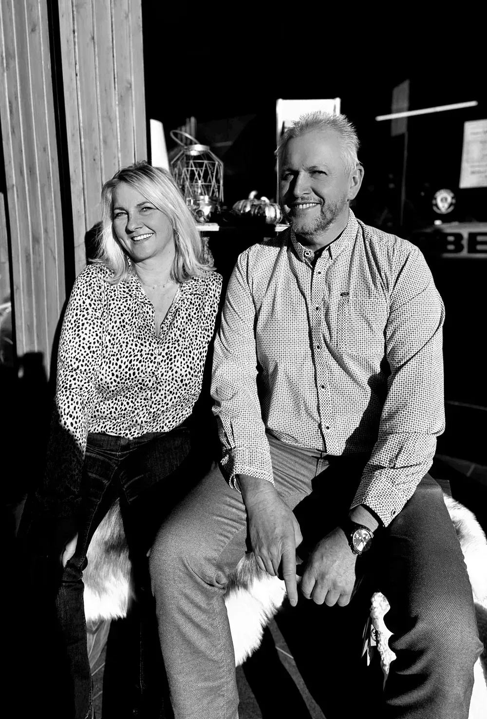 Ein lächelnder Mann und eine lächelnde Frau posieren gemeinsam in einem Innenraum. Sie tragen lässige gemusterte Hemden. Hinter ihnen ist ein Schild teilweise sichtbar.