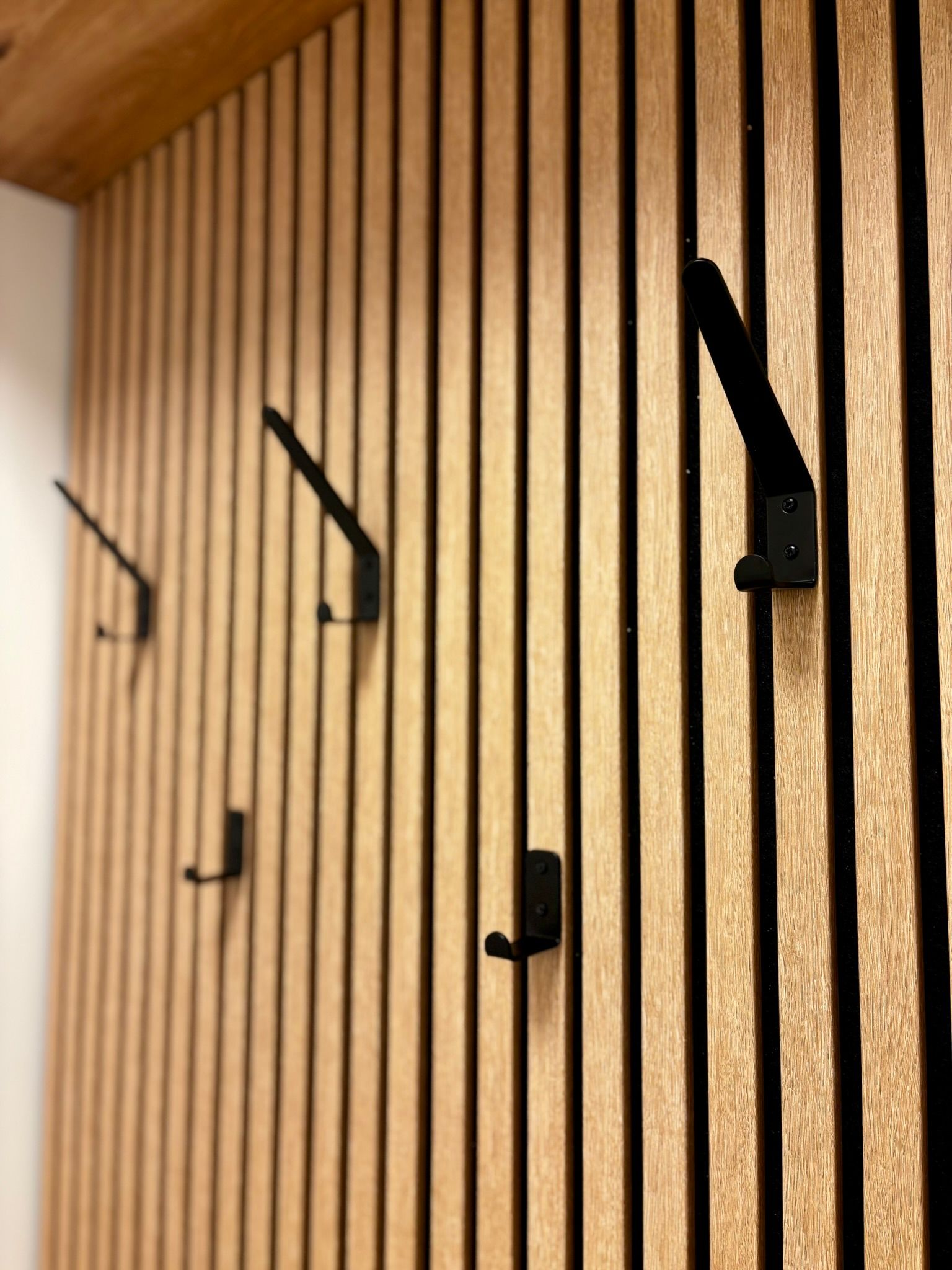 Schwarze Metallgarderobenhaken sind an einer dekorativen Wand aus vertikalen, hellen Holzlatten befestigt.