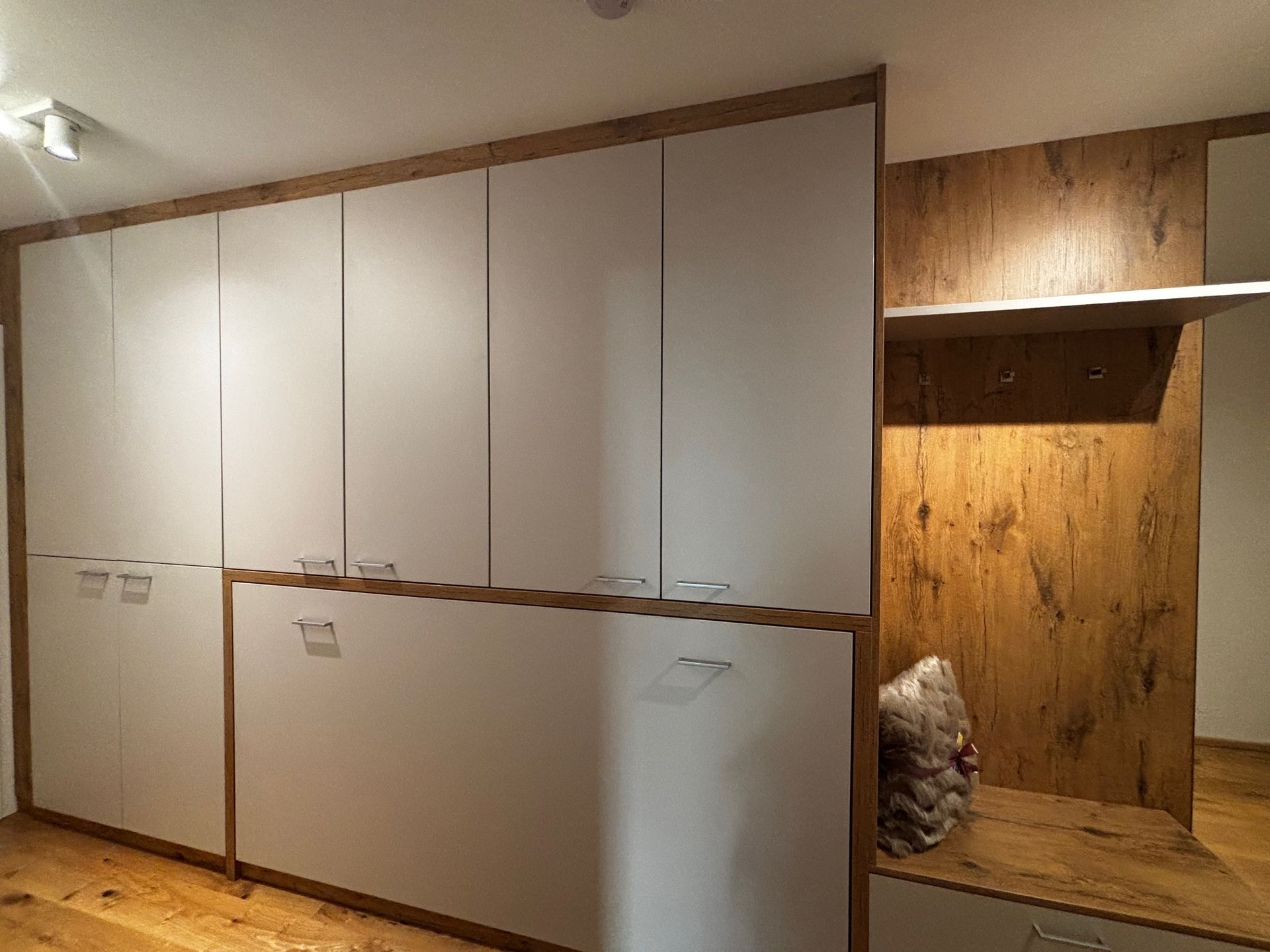 Ein raumhoher Holzschrank mit weißen Türen und einer integrierten Eingangsbank mit Haken und strukturierter Holzoberfläche.