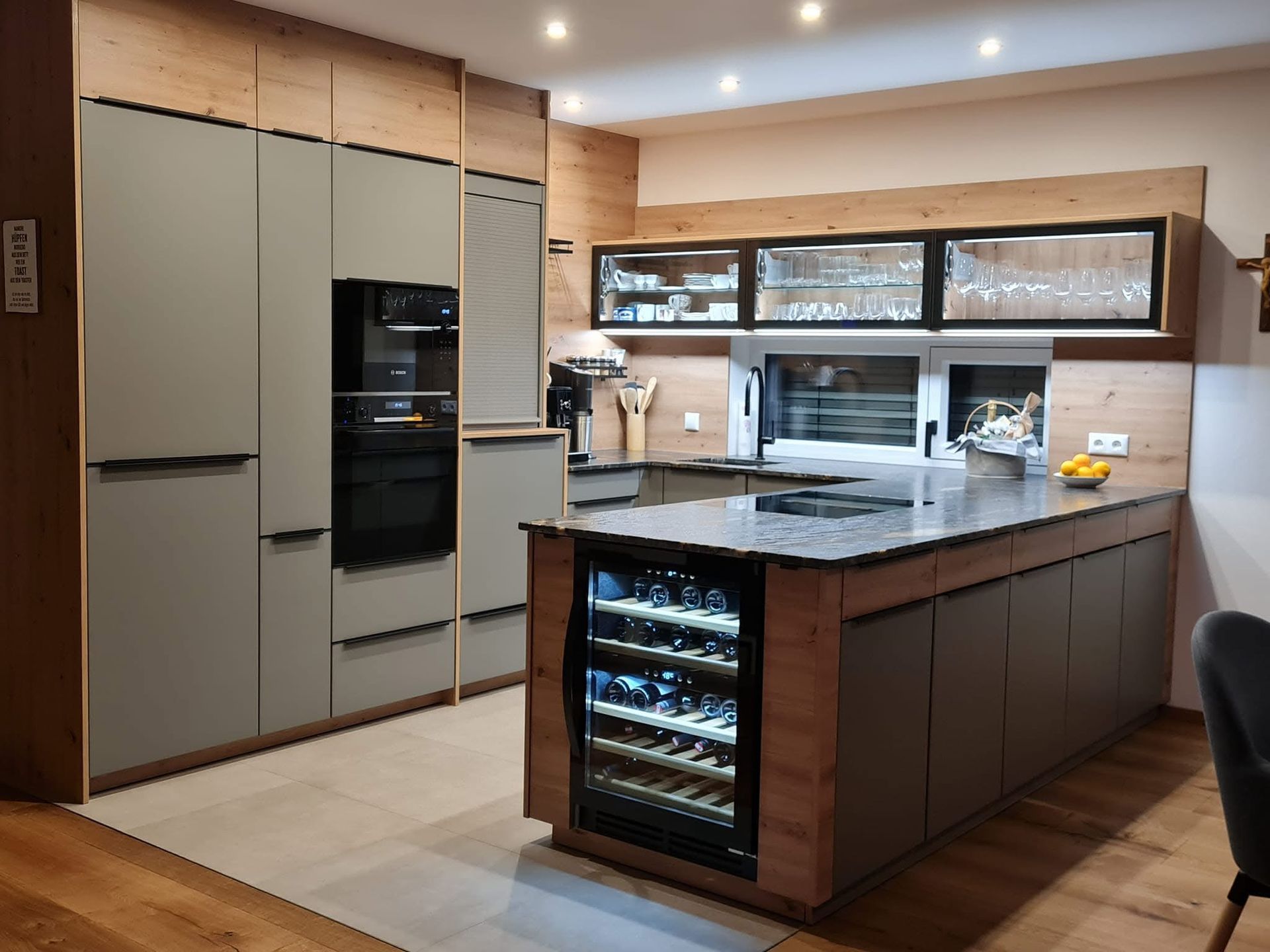 Moderne Küche mit salbeigrünen Schränken, hellen Holzelementen, einer Kücheninsel mit Marmorplatte und einem eingebauten Weinkühlschrank.