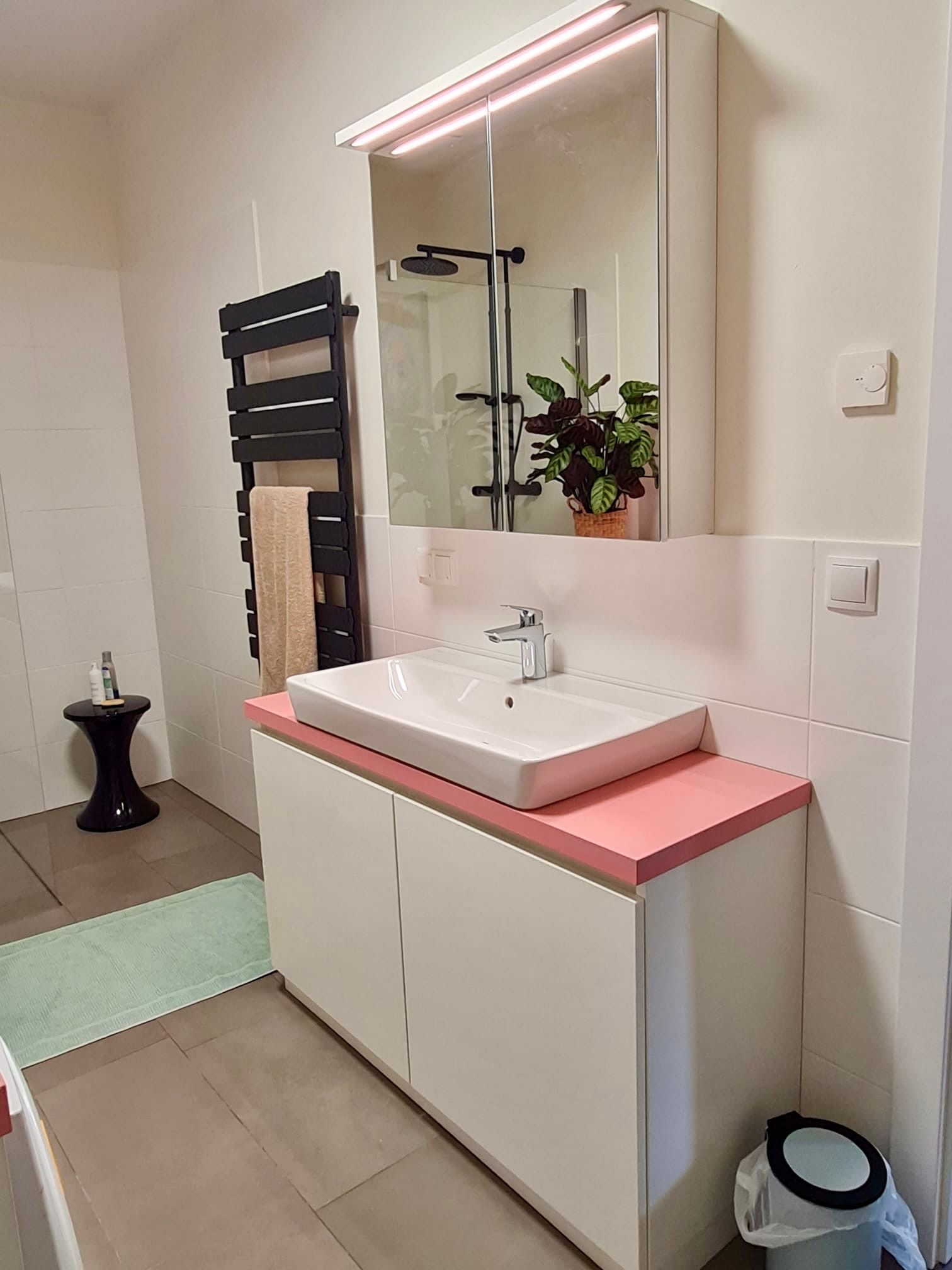 Ein modernes Badezimmer mit weißem Waschtisch mit rosa Arbeitsplatte, Aufsatzwaschbecken und beleuchtetem Spiegelschrank.