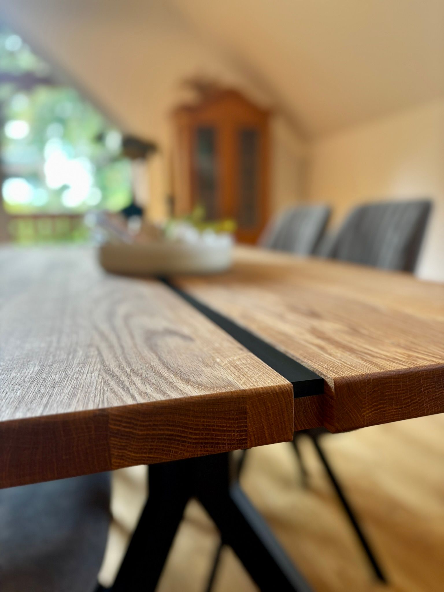 Nahaufnahme eines hölzernen Esstisches mit schwarzer Mitteleinlage und modernen Metallbeinen in einem verschwommenen Raum.