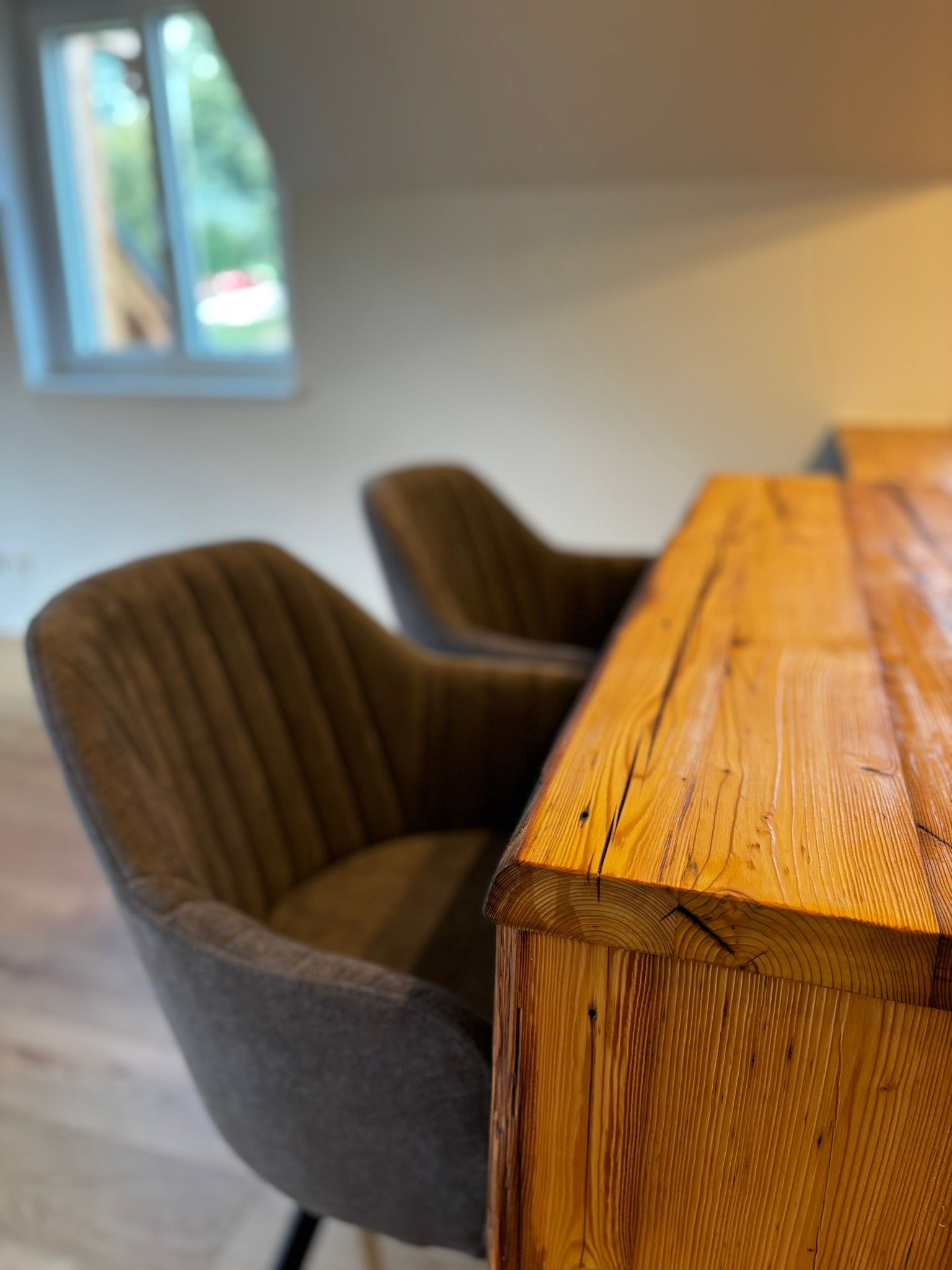 Zwei graue, gerippte Polsterstühle stehen unter einem rustikalen Holzschreibtisch in einem hell erleuchteten Zimmer mit Fenster.
