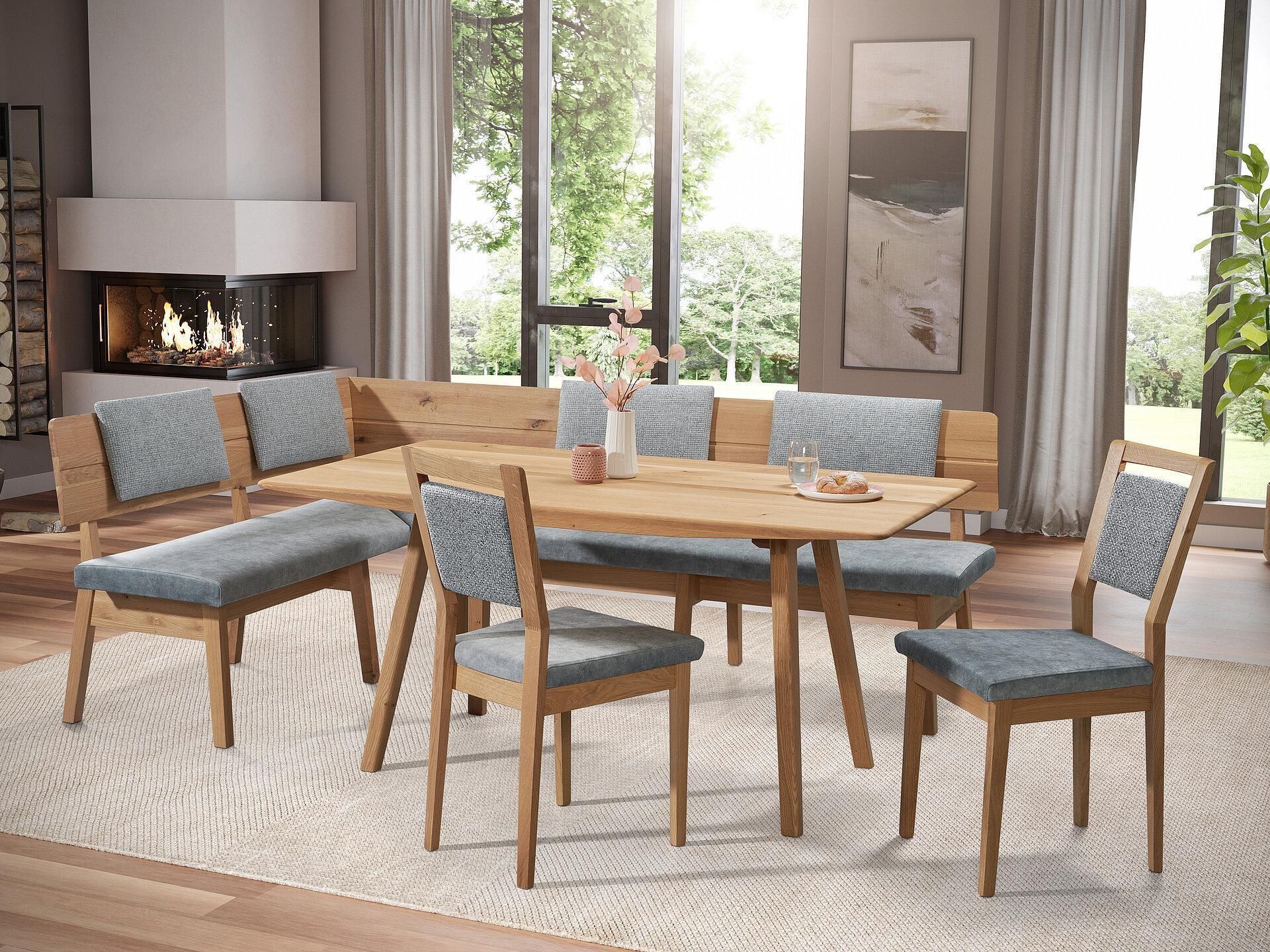 Esszimmergarnitur mit einer L-förmigen Holzbank und zwei Stühlen, alle mit hellblauen gemusterten Kissen auf einem Teppich.