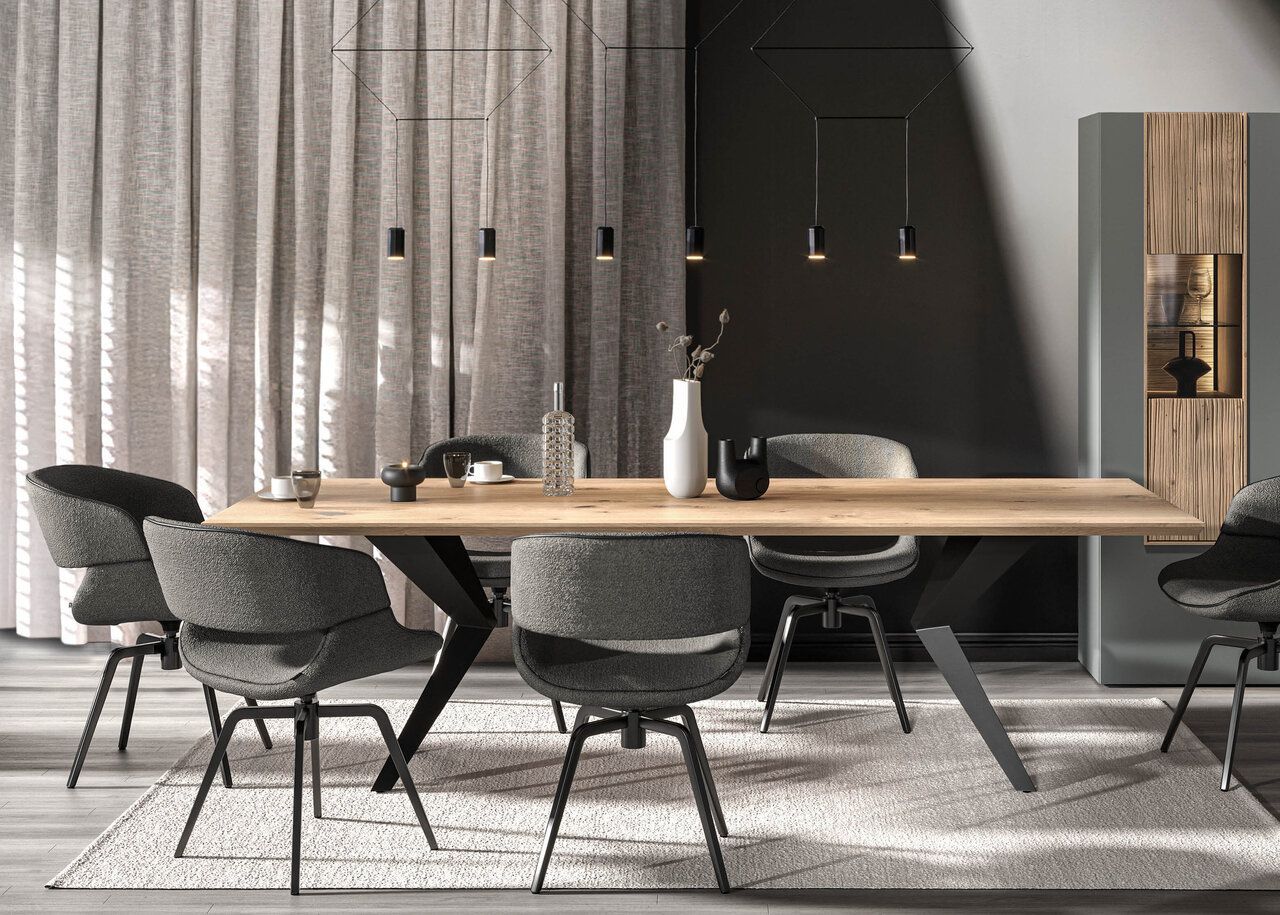 Ein modernes Esszimmer mit einem langen hellen Holztisch, schwarzen Metallbeinen und sechs grauen, strukturierten Drehstühlen auf einem hellen Teppich.