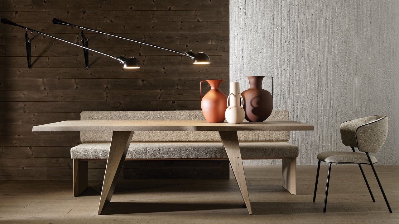 Ein Esszimmer mit einem Holztisch, einer gepolsterten Bank und einem Stuhl, beleuchtet von zwei Wandlampen vor einer strukturierten Wand.