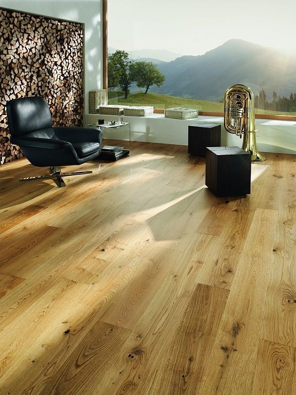 Ein modernes Wohnzimmer mit hellen Holzböden, einem dunklen Ledersessel und einem großen Fenster mit Blick auf die Berge.