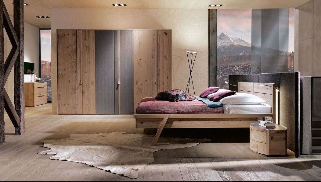 Ein modernes Schlafzimmer mit Holzbett, großem Kleiderschrank und Bergblick durch ein Fenster, gestaltet in warmen, natürlichen Farbtönen.