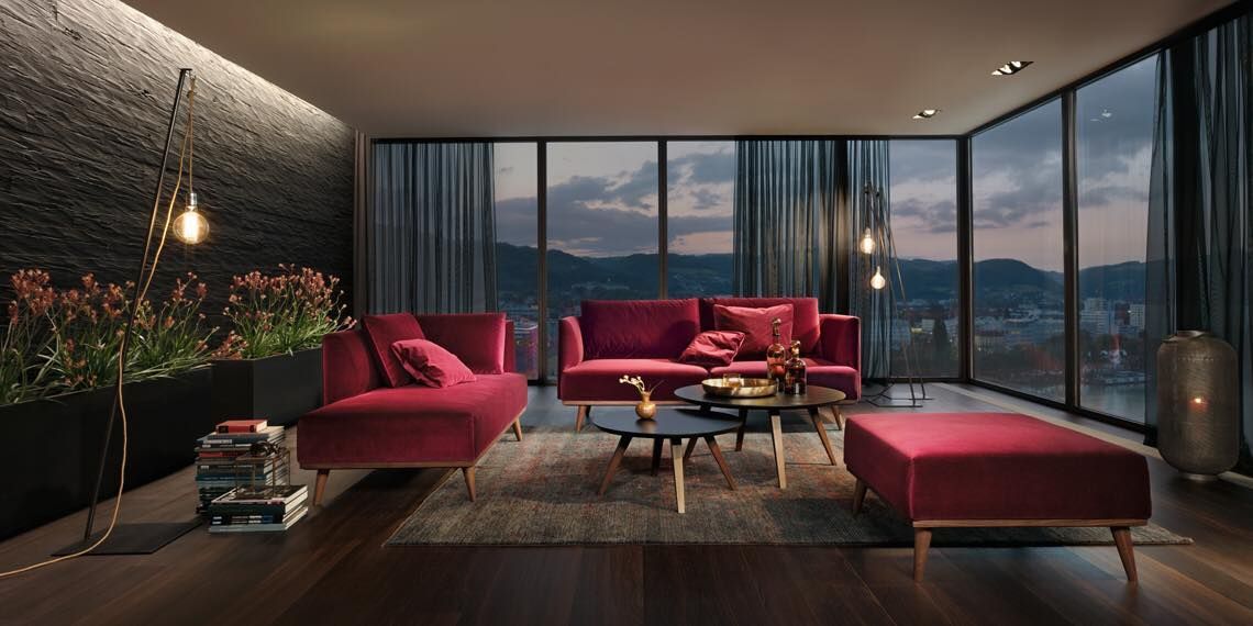 Modernes Wohnzimmer mit burgunderroten Samtsofas, passendem Ottoman, einer strukturierten schwarzen Wand und bodentiefen Fenstern.