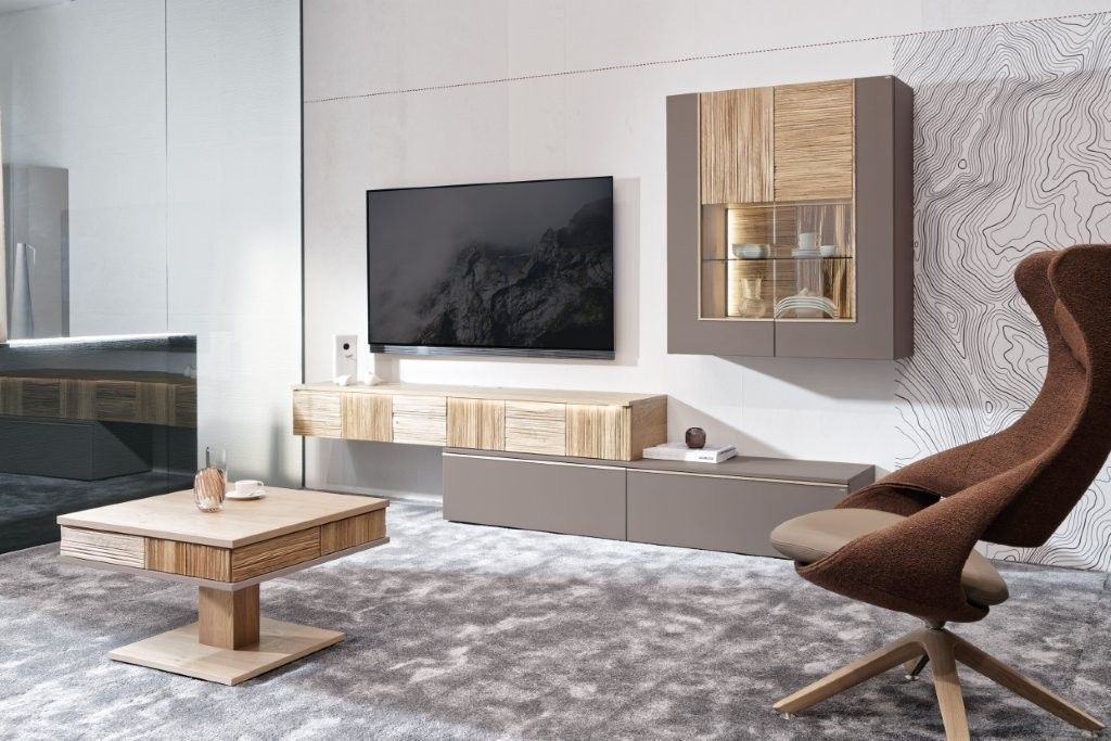 Modernes Wohnzimmer mit Fernseher, schwebenden Holzschränken, niedrigem Couchtisch und Sessel auf einem gemusterten grauen Teppich.