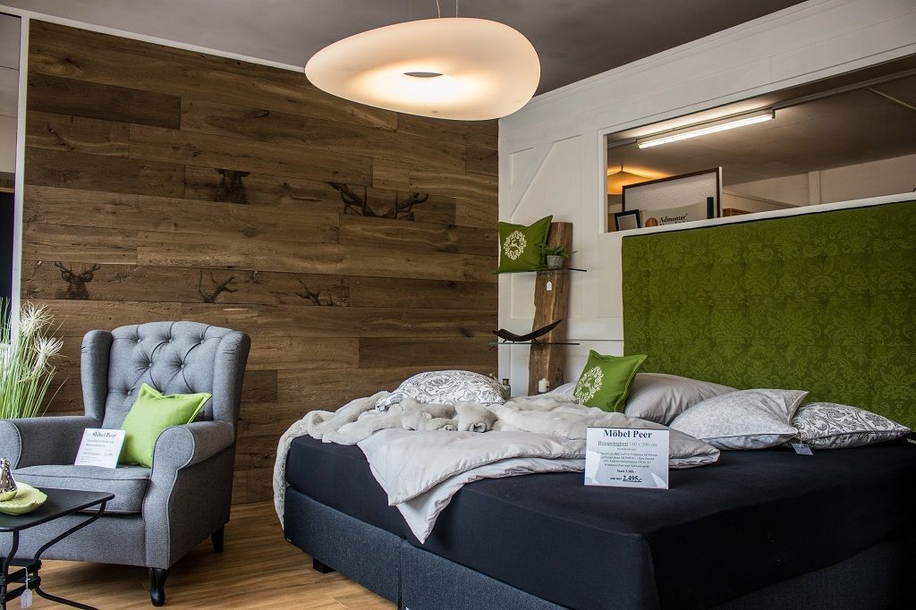 Ein gemütliches Schlafzimmer mit einem gesteppten grauen Sessel, einem großen schwarzen Bett mit mehreren Lagen Bettwäsche und einer moosgrünen Kopfteilwand.