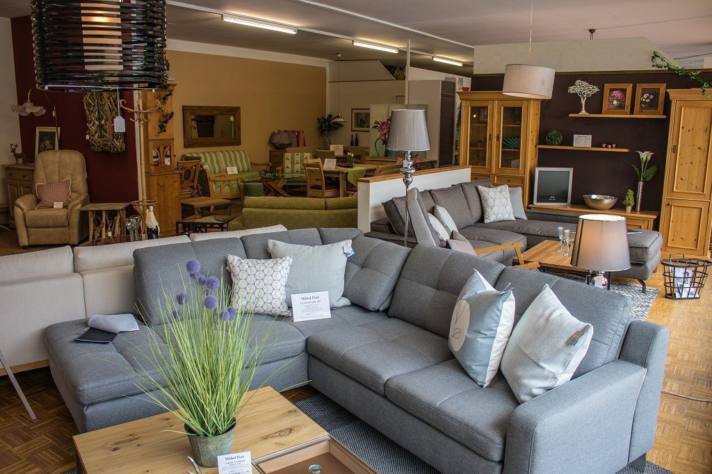 In einem Möbelhaus sind graue Ecksofas, Couchtische aus Holz und verschiedene Wohnaccessoires ausgestellt.