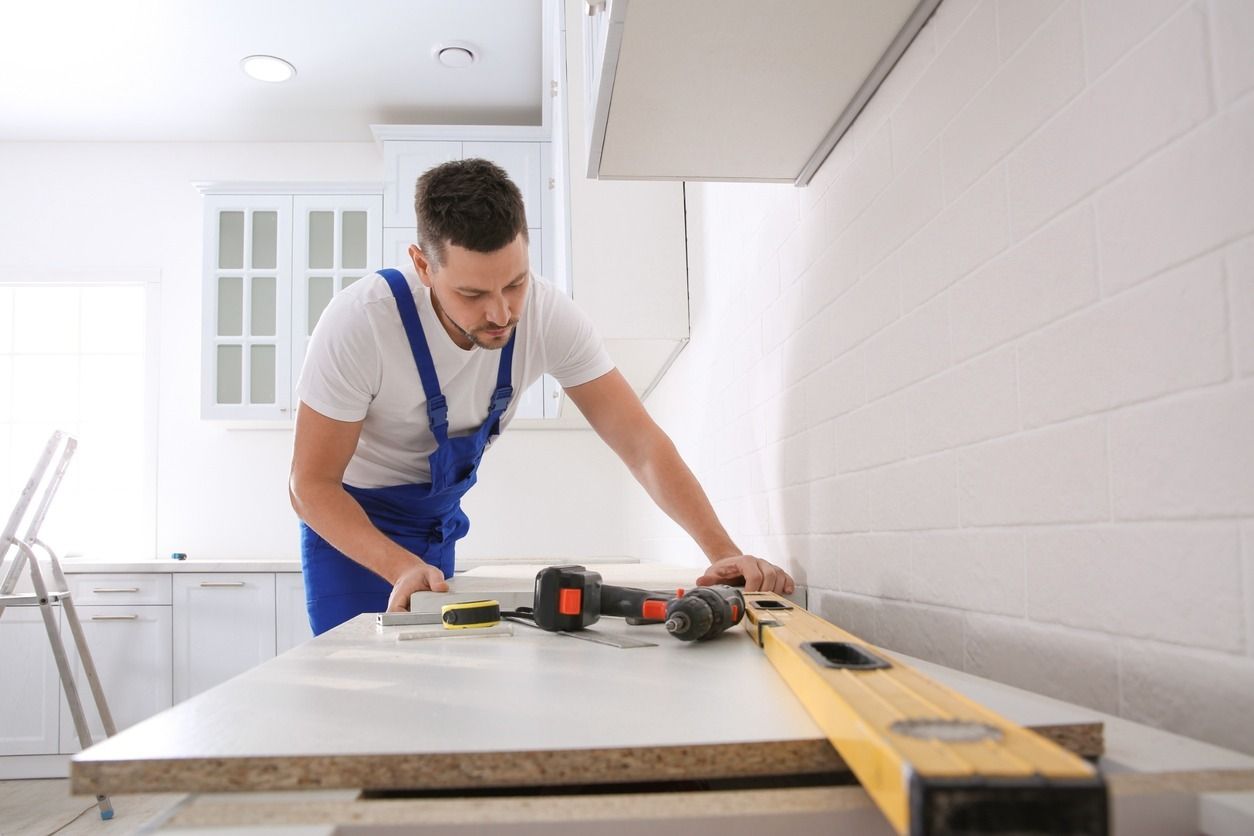 Un hombre con un mono azul usa un nivel sobre una encimera de una cocina blanca, probablemente para instalarlo.