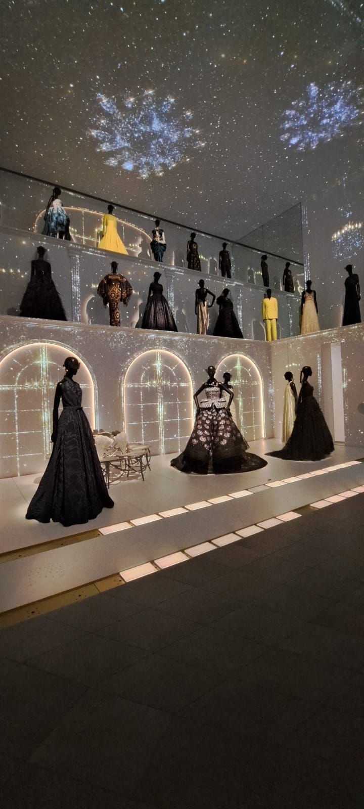 Des mannequins présentent des robes de soirée dans un espace galerie orné d'arches