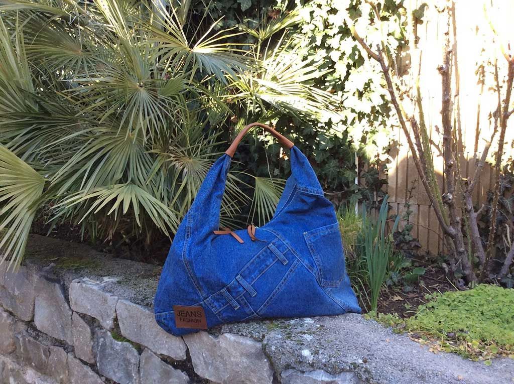Un sac cabas en denim bleu posé sur un rebord de pierre dans un jardin, à côté de palmiers.