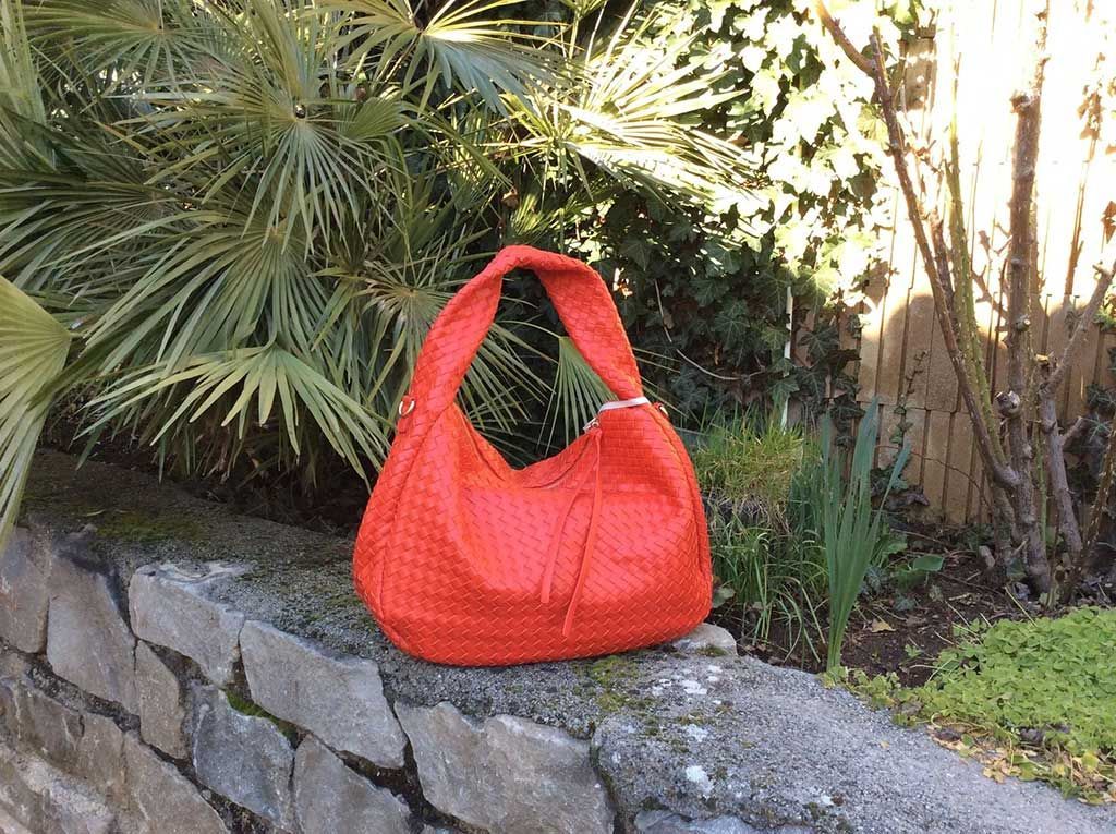 Sac à main rouge vif sur un muret en pierre dans un jardin verdoyant