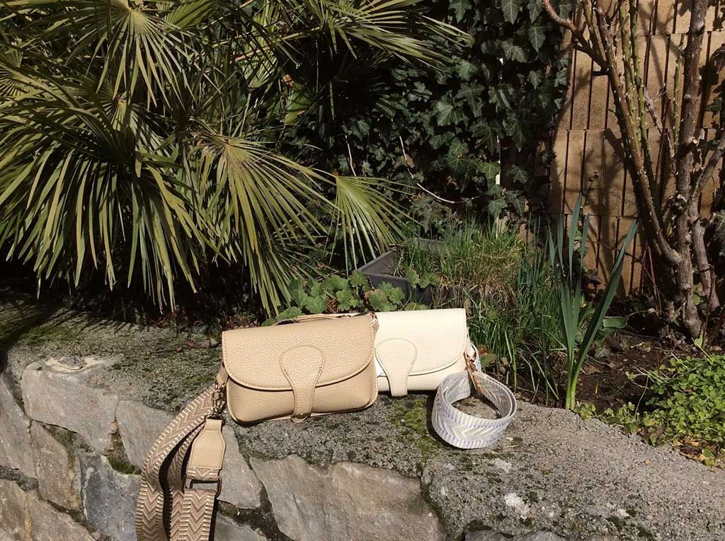 Sac à main beige et chaussures argentées sur un rebord de pierre dans un jardin