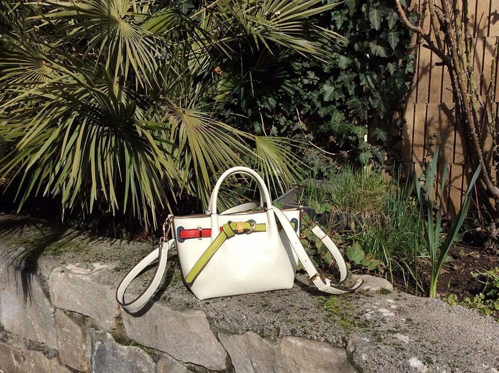 Sac à main blanc posé sur un muret de pierre, à côté de verdure et de feuilles de palmier.