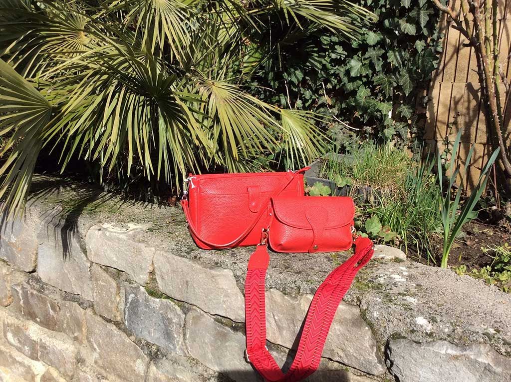 Sac à main rouge sur un muret de pierre, près de palmiers, au soleil