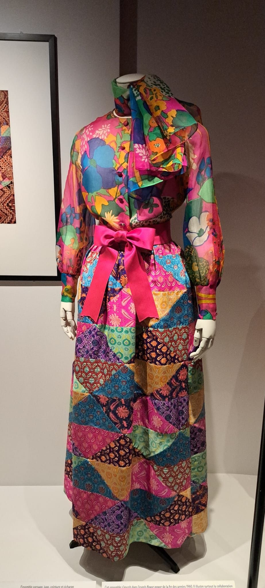 Un mannequin qui porte une robe longue en patchwork multicolore, ornée d'une ceinture à nœud rose