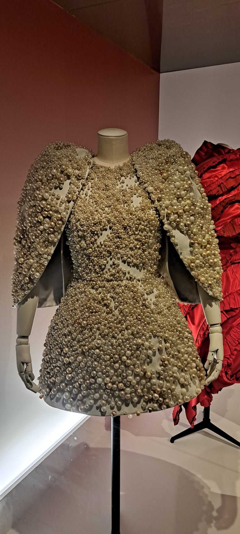 Une robe courte texturée couleur crème, à manches ailées, présentée sur un mannequin dans un musée