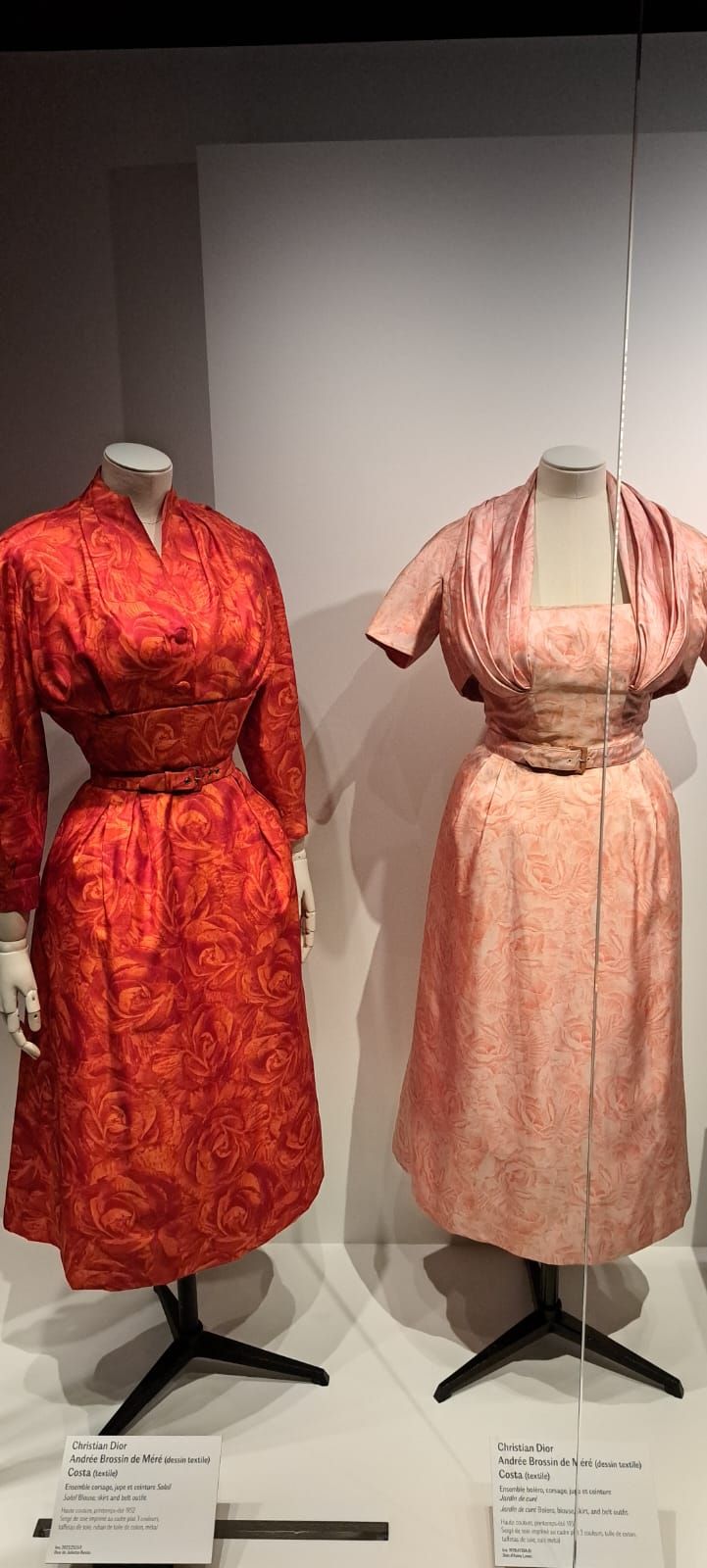 Deux mannequins présentent des robes vintage à motifs rouges et rose pâle dans une mise en scène de galerie