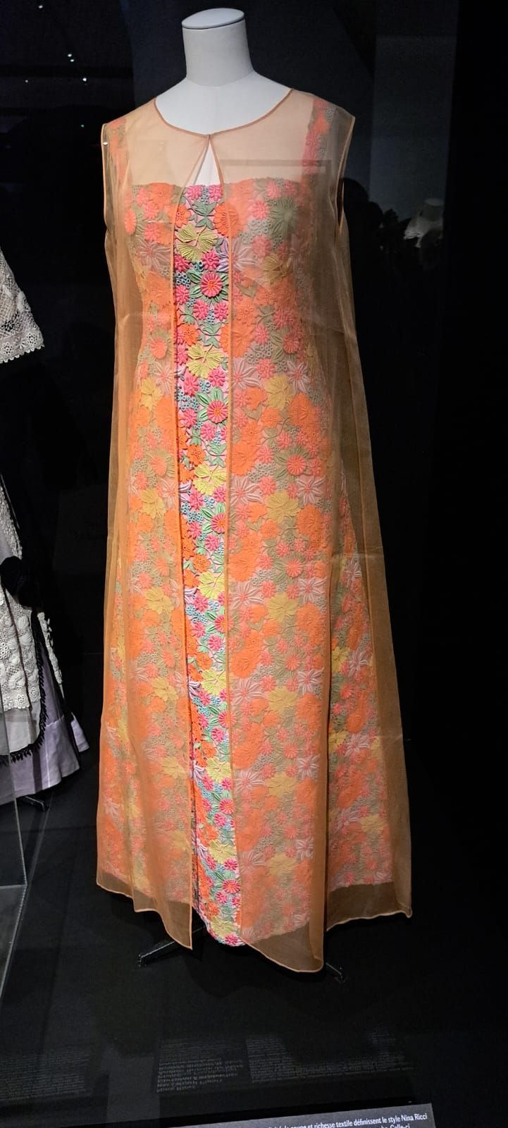 Une robe orange longue jusqu'au sol, à motifs floraux et à voile transparent, présentée sur un mannequin