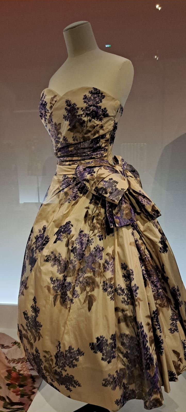 Robe de soirée bustier couleur crème avec imprimé floral violet et  grand nœud à la taille, présentée sur un mannequin