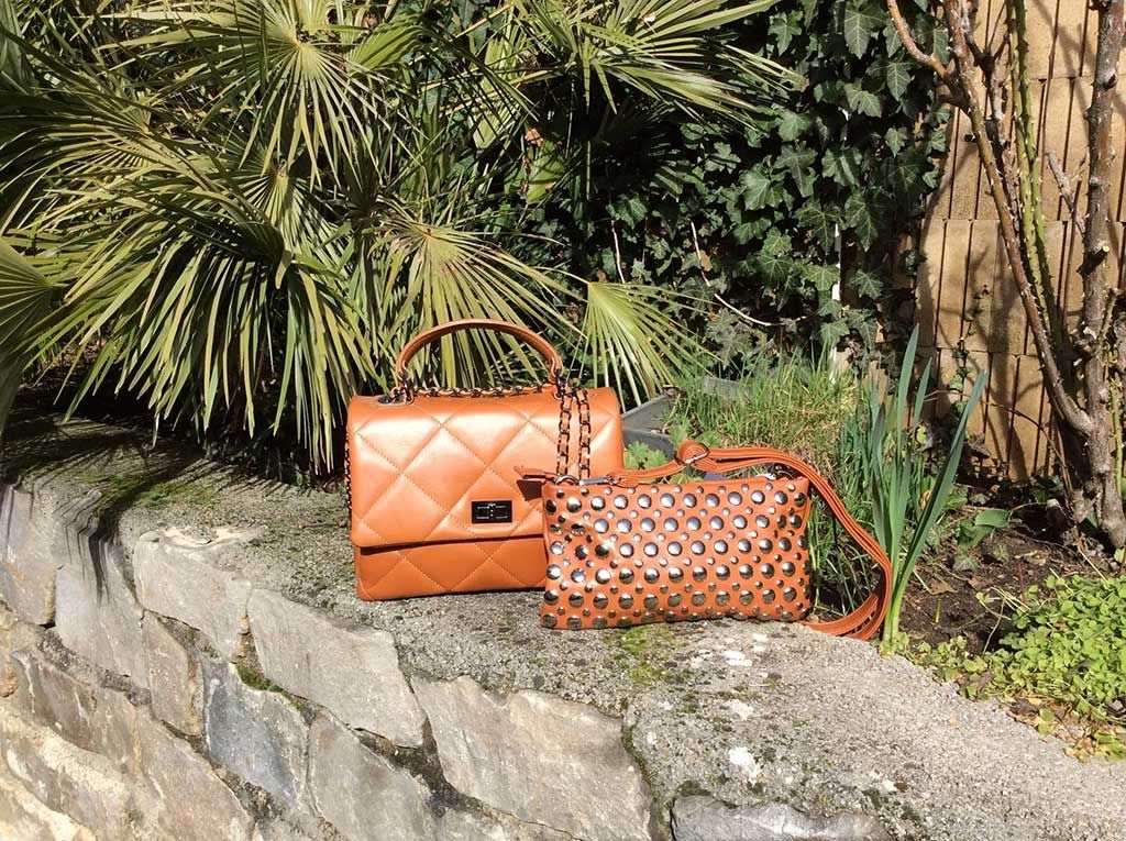Deux sacs à main orange sur un muret en pierre dans un jardin verdoyant