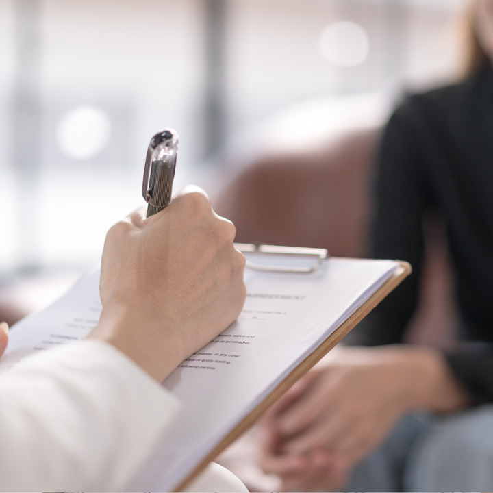 Escritura a mano en un portapapeles, entrevistando a alguien en un entorno de oficina.