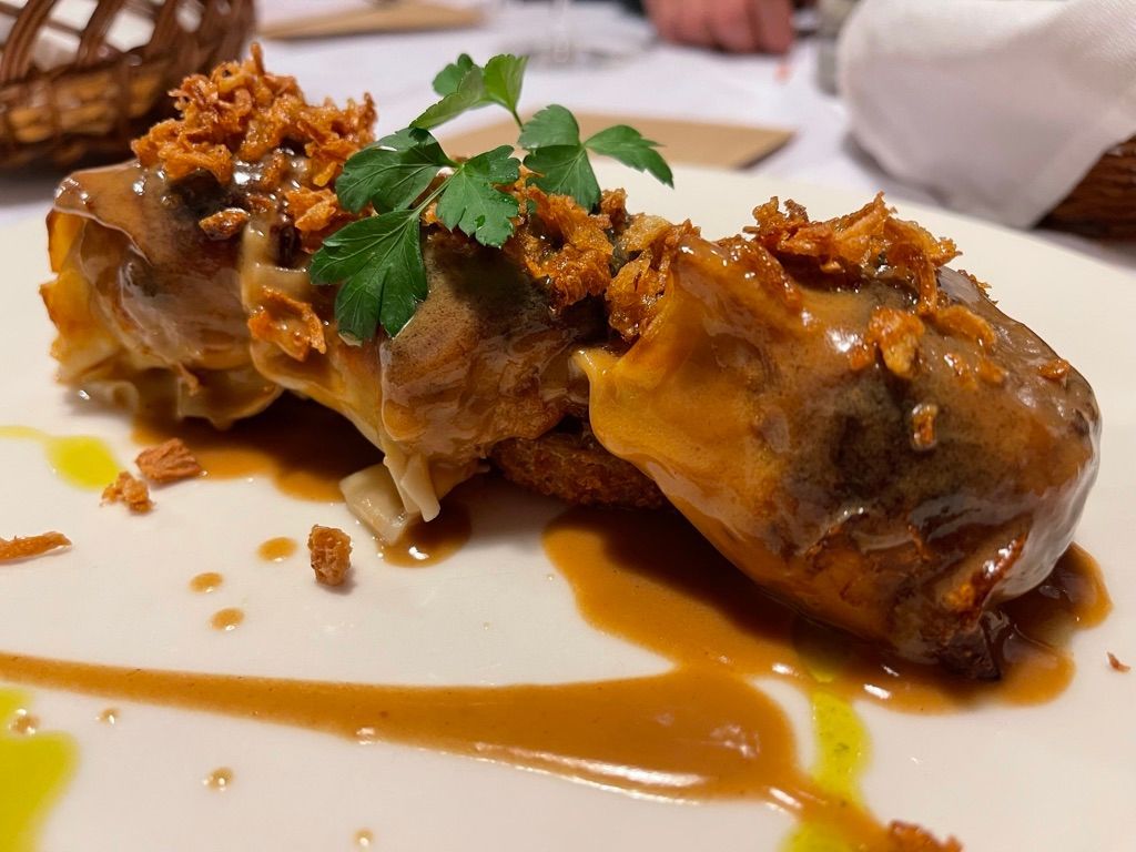 Tres porciones de comida enrolladas con salsa, adornadas con nueces y perejil, en un plato blanco.