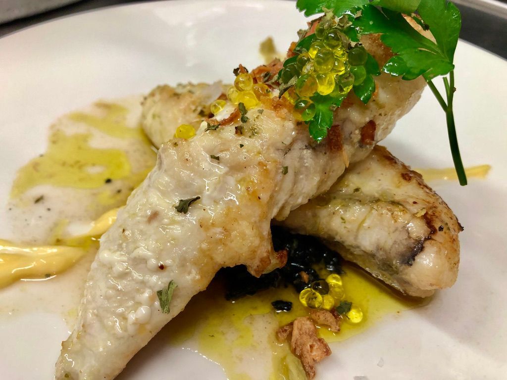 Pescado blanco salteado con guarnición, salsa amarilla y aceite de oliva en un plato blanco.