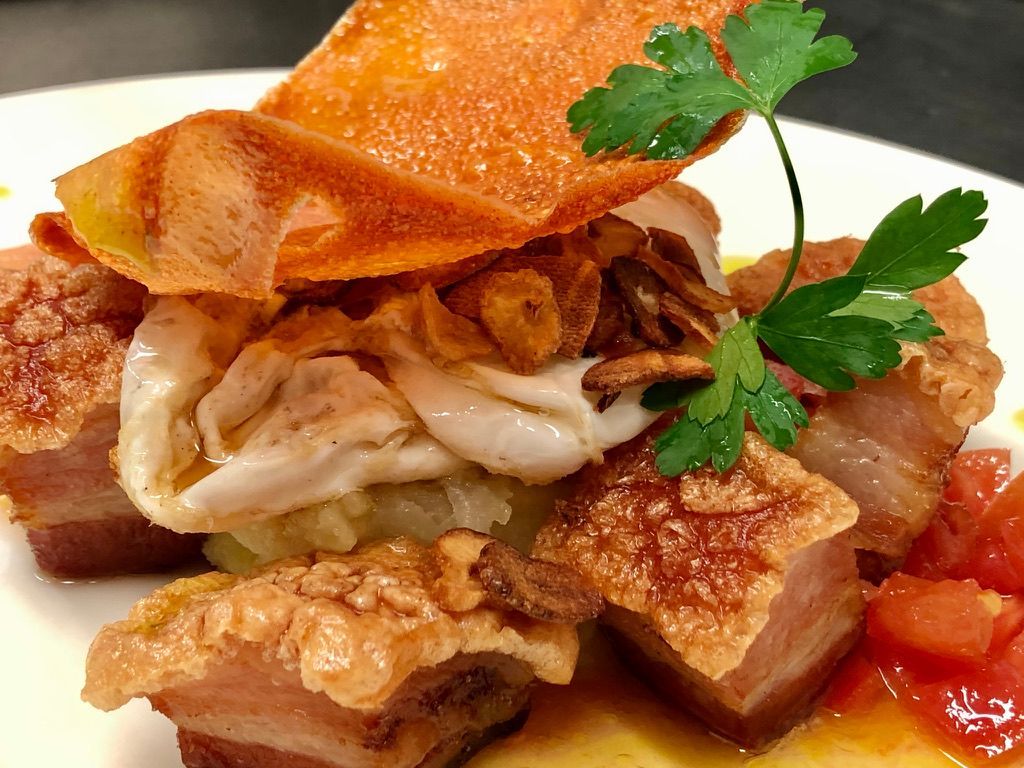 Cubitos de panceta de cerdo crujientes con chicharrón, ajo frito, tomate y perejil.