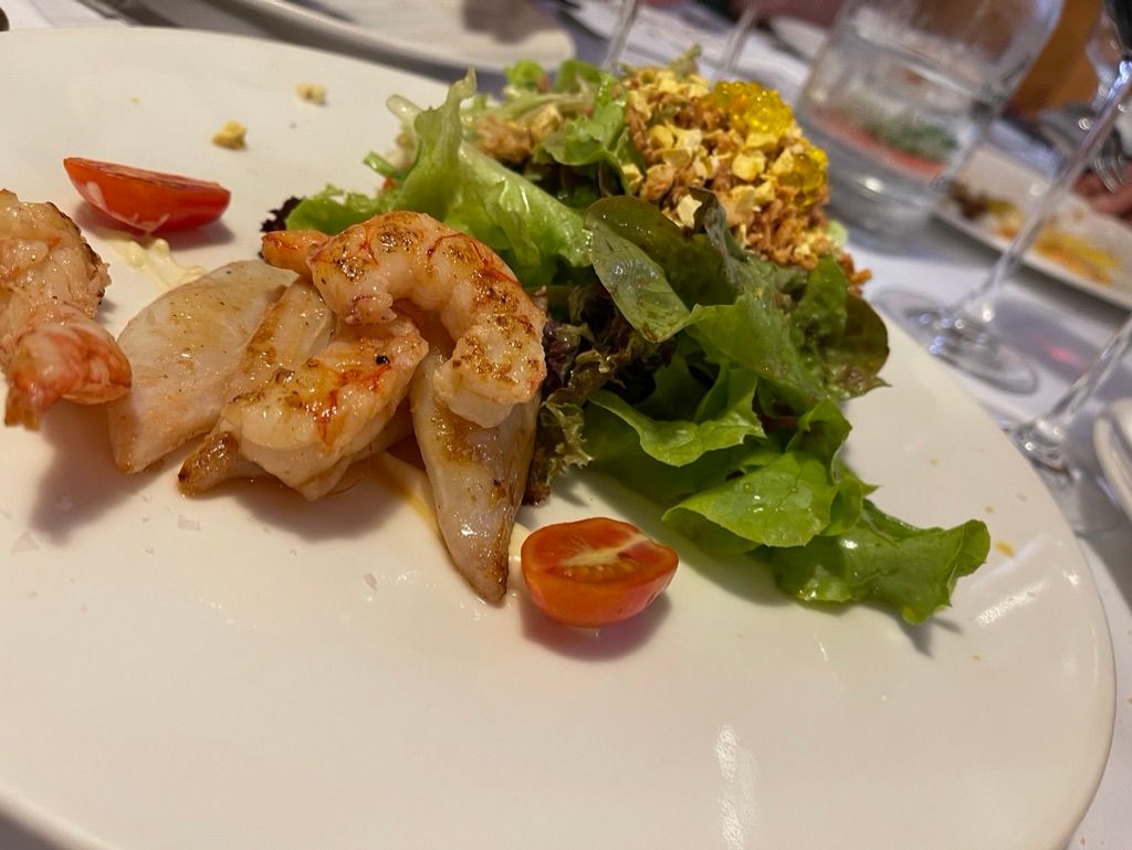 Camarones y vieiras a la parrilla con ensalada y tomates en un plato blanco.