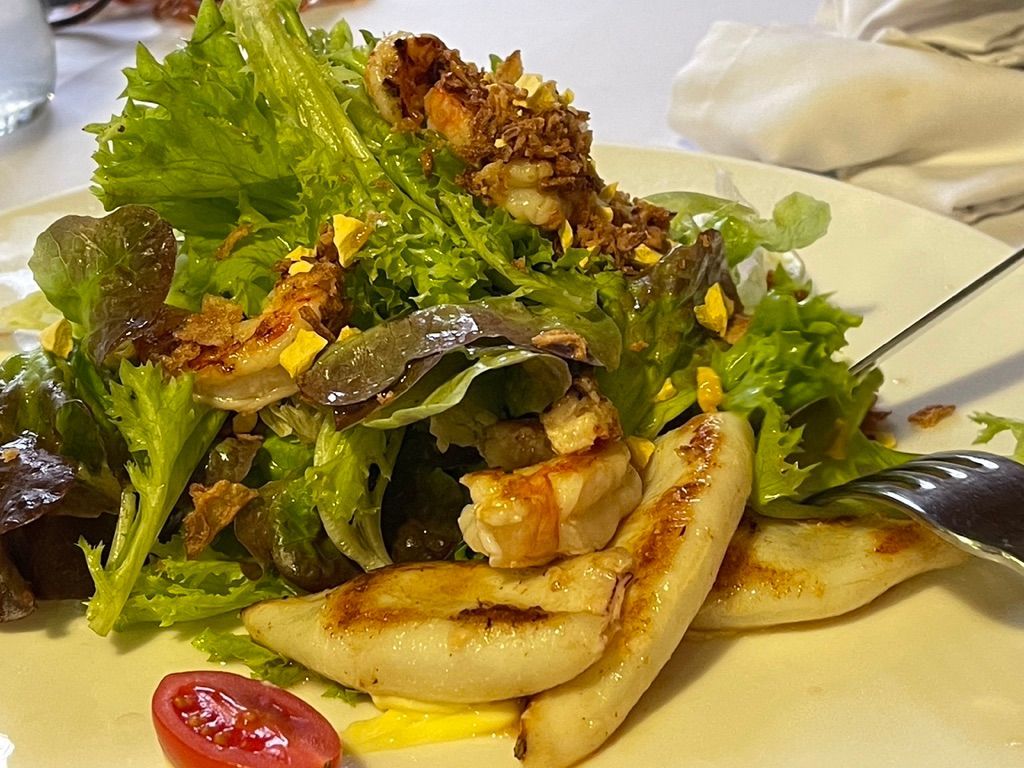 Ensalada con setas ostra a la parrilla, verduras y nueces tostadas en un plato blanco.