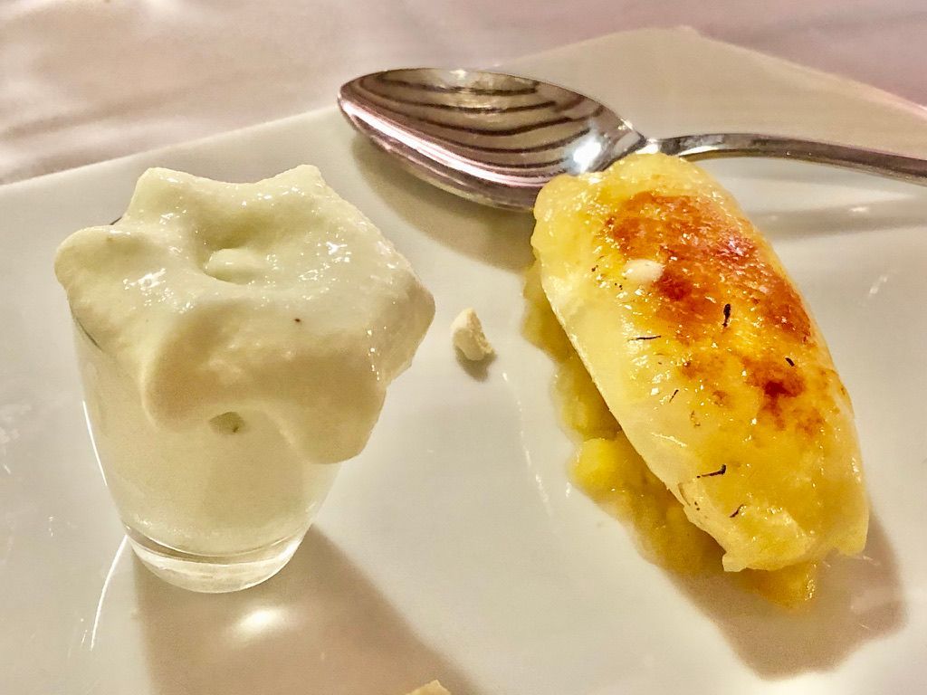 Plato de postre con helado blanco en vaso y fruta caramelizada; cuchara reposa en el plato.