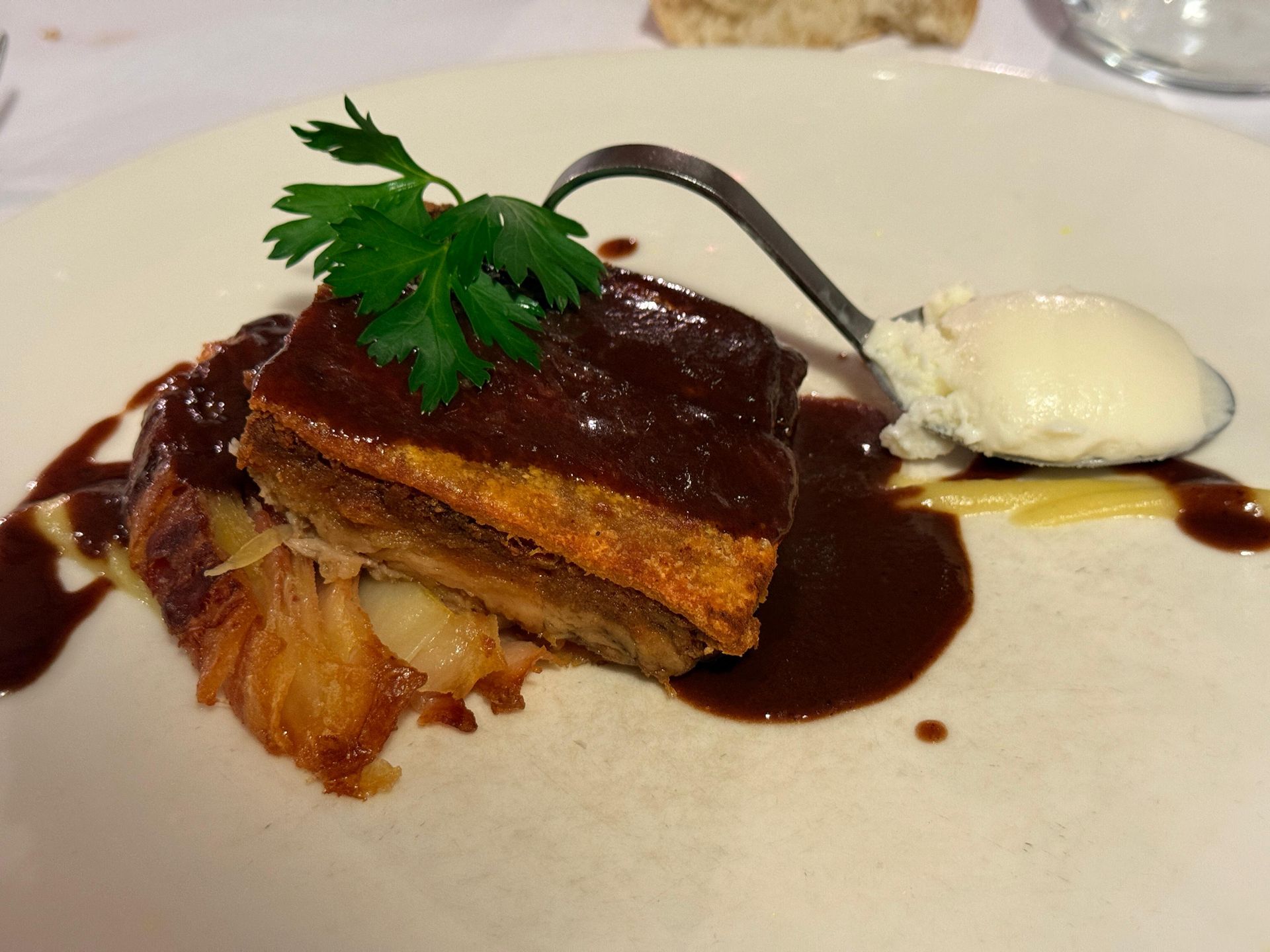 Panceta de cerdo estofada con salsa, perejil y helado en un plato blanco.