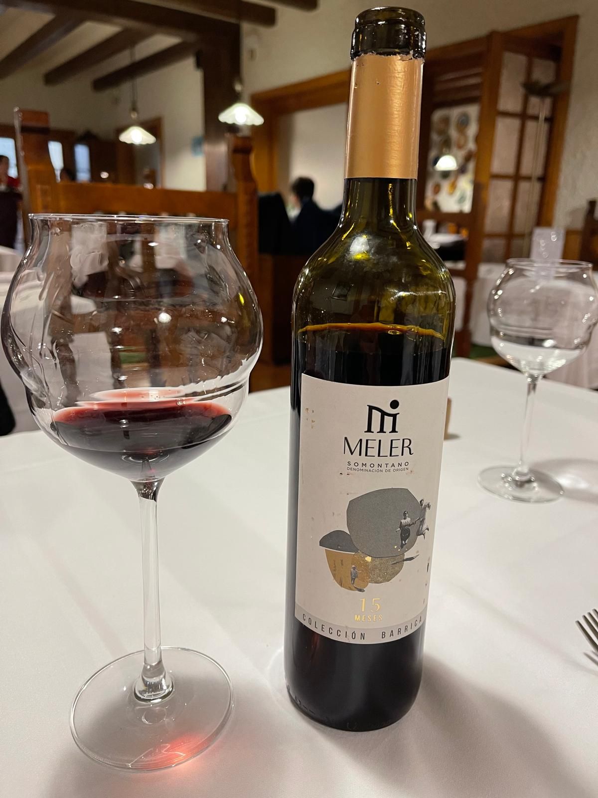 Una botella y una copa de vino sobre una mesa, con vino tinto a la vista.