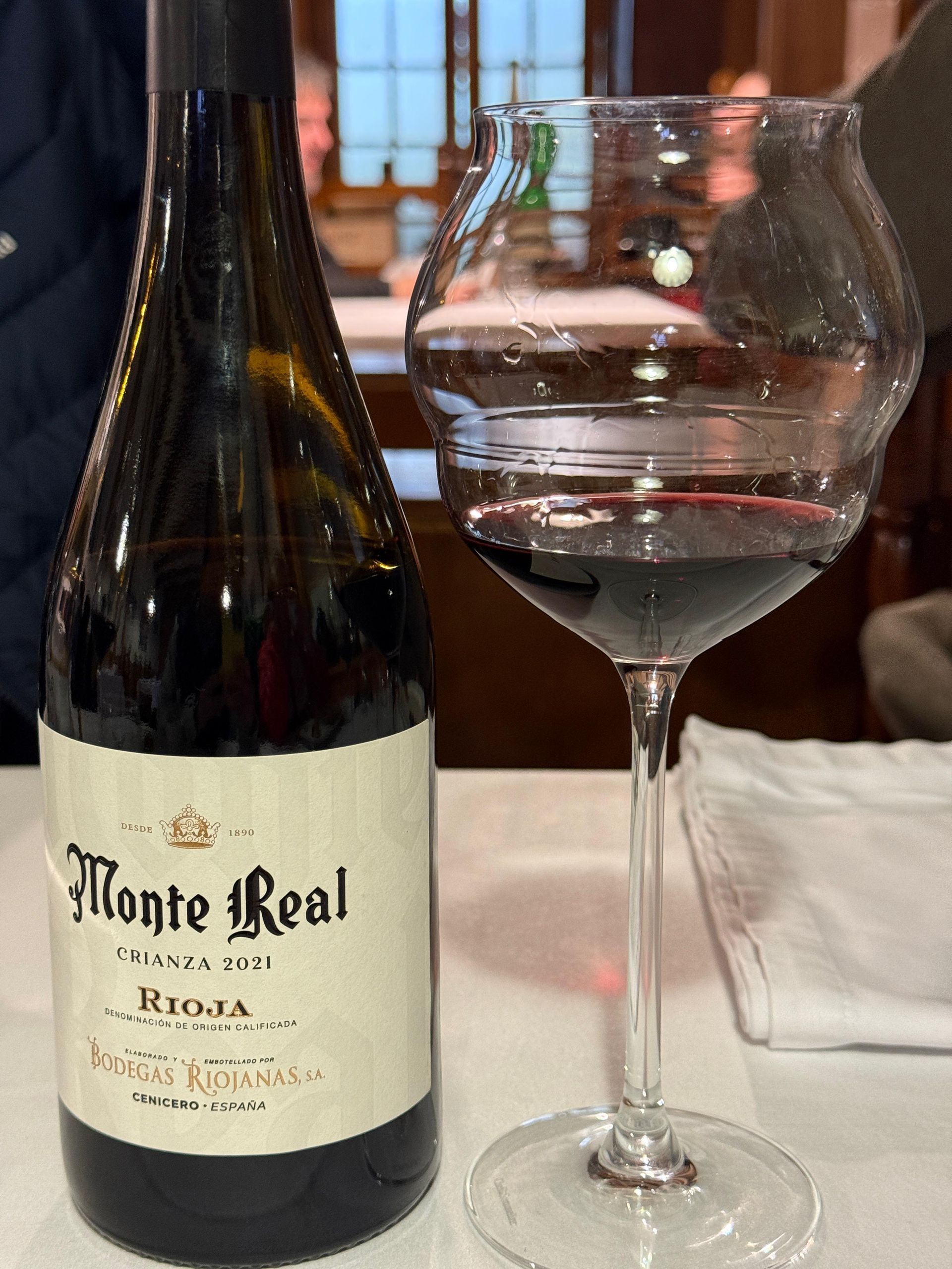Botella de vino Monte Real Rioja junto a una copa de vino tinto en una mesa.