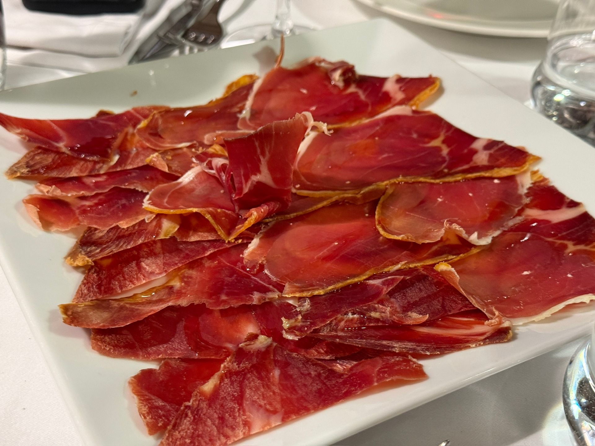 Jamón curado cortado fino en un plato blanco, entorno de restaurante.