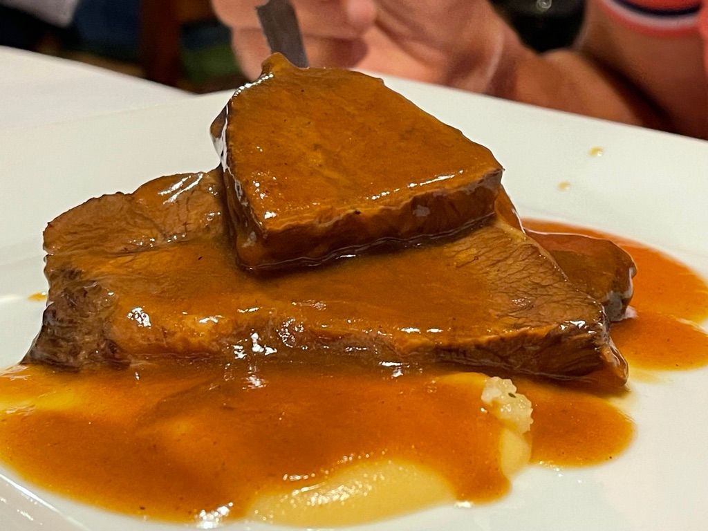 Carne de res asada cortada en rodajas con salsa en un plato blanco, levantando un trozo con un tenedor.