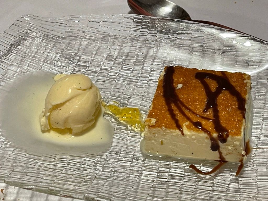 Postre en plato transparente: helado de vainilla, salsa de caramelo y un cuadradito de crema pastelera.