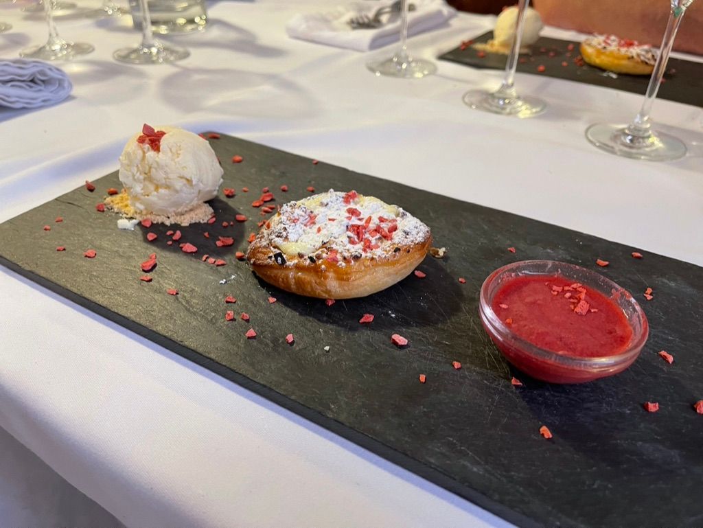 Plato de postre con hojaldre, helado y salsa roja. Mantel blanco.