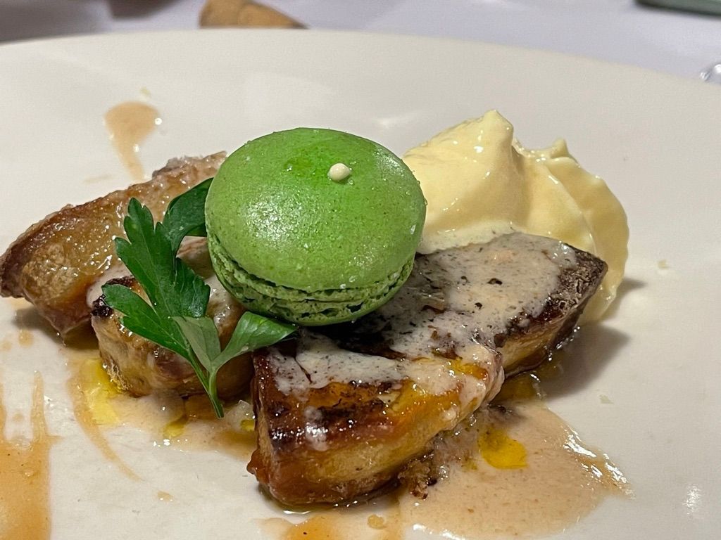 Foie gras sellado con macaron verde, perejil y crema, en un plato blanco.