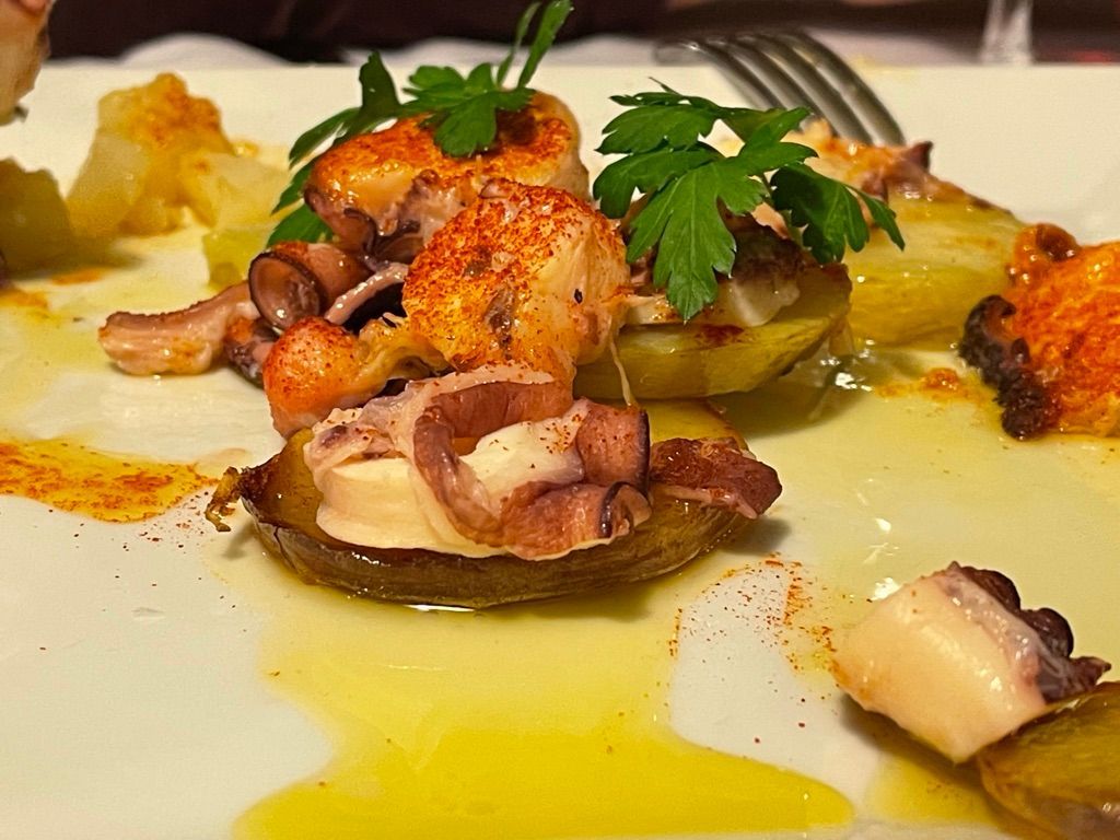 Plato de pulpo y patatas con pimentón y perejil en plato blanco.
